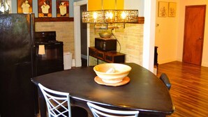 A kitchen with a black refrigerator, a microwave, and a stove. There is a dining table with a bowl on it and two white chairs. A hanging light fixture is above the table. - Riverside : delightful ambiance and ample natural light makes a unique place (Grand Forks)
