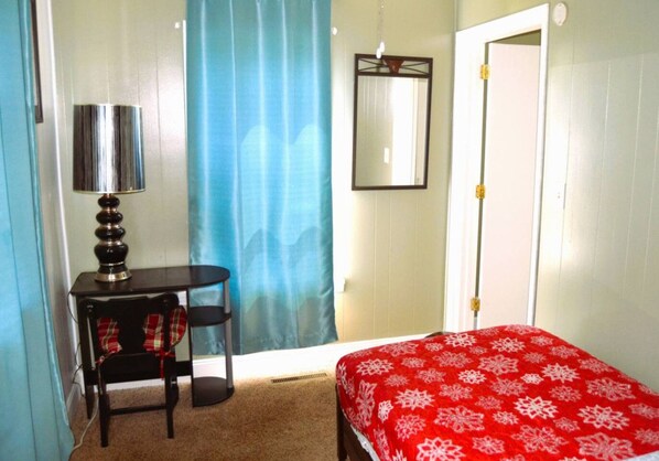 A bedroom with a bed, a desk, a chair, a lamp, and a door.