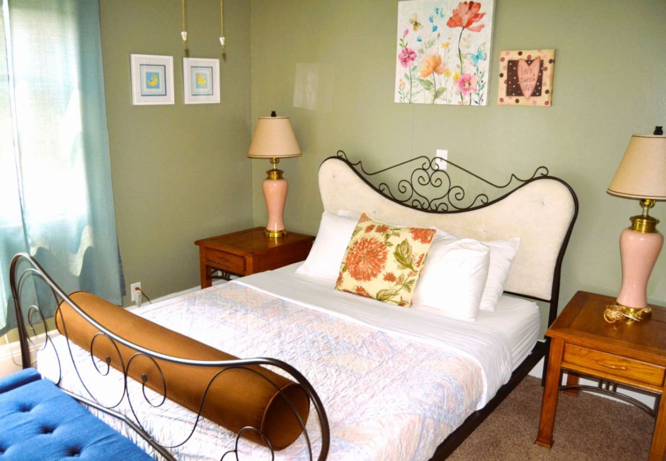 A neatly arranged bedroom with a bed, two bedside tables, a nightstand, and a blue chair.