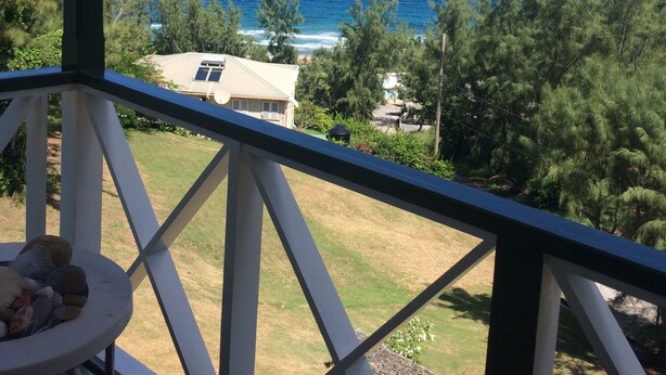 A balcony with a view of the ocean and a house in the background.