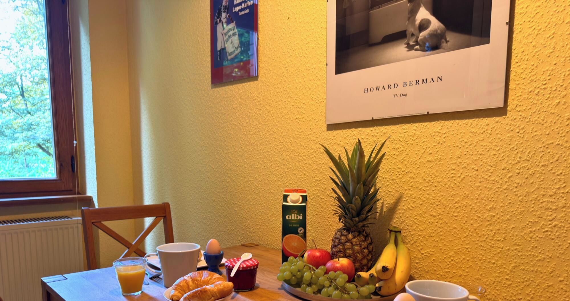 Ein Frühstückstisch mit einem Croissant, Obst, einem Glas Saft und einer Orangensaftpackung.