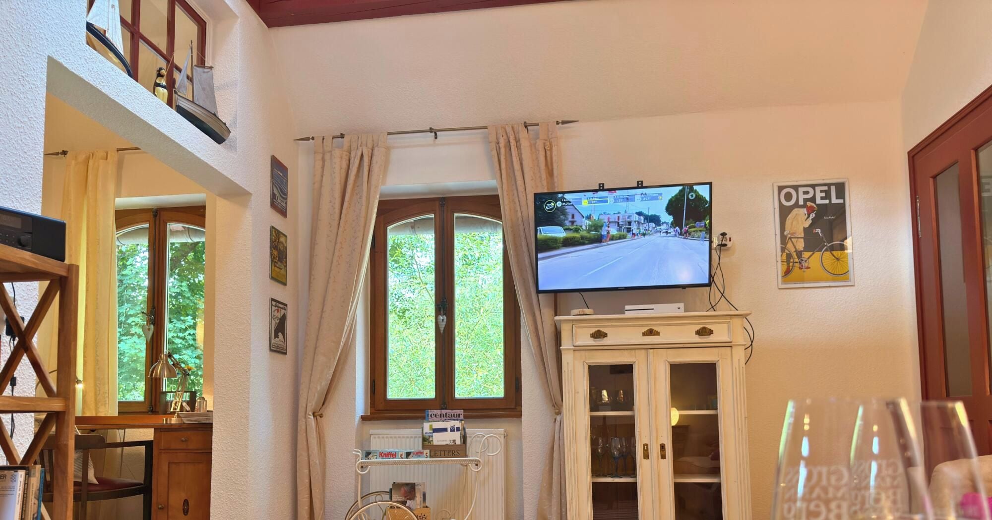 Ein Zimmer mit Fernseher auf einem Schrank, einem Fenster mit Vorhängen und einem Poster an der Wand.