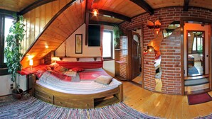 Une pièce circulaire et chaleureuse, avec des murs en bois, un lit, une cheminée en briques et un petit coin salon.