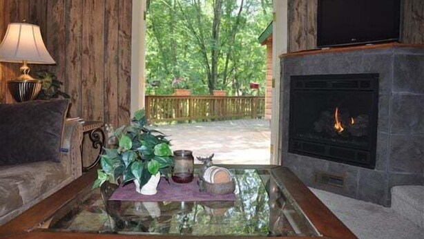 A living room with a fireplace, a television, and a view of a wooden deck and trees.