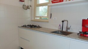 Une cuisine avec des meubles blancs, un plan de travail en granit, une cuisinière à gaz, un évier et des casseroles suspendues.