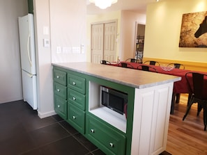 A kitchen with green cabinets, a built-in microwave, and a dining area with a red tablecloth.