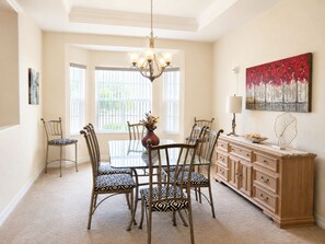 A dining room with a glass table, patterned chairs, a wooden cabinet, and a chandelier. - Modern Bright Contemporary Design 2,400 SF of comfort with Salt Pool & Spa, WiFi (North Port)