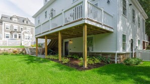 A two-story white house with a covered porch and a stone foundation. - Newly renovated pet friendly apt by parks and train! (Boston)