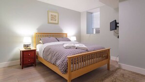 A bedroom with a wooden bed, bedside tables with lamps, a wall-mounted TV, and a framed picture. - Newly renovated pet friendly apt by parks and train! (Boston)