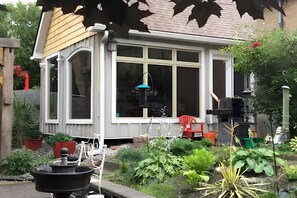 A small house with a large window, a garden with various plants, and a red chair outside.