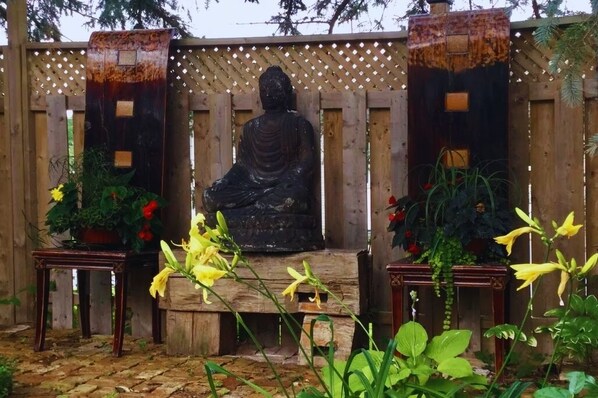 A statue of a seated figure in a garden setting with wooden structures and potted plants.
