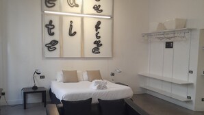 Une chambre d’hôtel avec un lit, un fauteuil noir, une table de chevet, une lampe et une armoire.