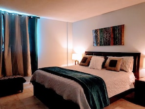 Uma cama bem arrumada com um edredom verde escuro, cabeceira de madeira e várias almofadas.