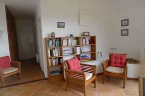 Une pièce avec une bibliothèque en bois remplie de livres, deux chaises en bois avec des coussins et un sol carrelé.