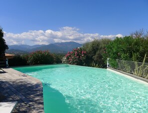 Une piscine à l’eau turquoise et cristalline, entourée d’une végétation luxuriante et de fleurs roses.