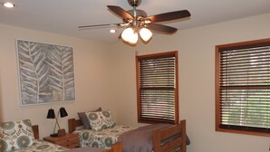 Un dormitorio con dos camas de madera, un ventilador de techo y un gran ventanal con persianas.