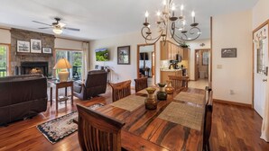 A spacious living room with a fireplace, a dining area with a wooden table and chairs, and a kitchen in the background.