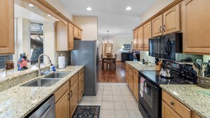 A kitchen with wooden cabinets, granite countertops, a stainless steel refrigerator, a black microwave, and a stove.