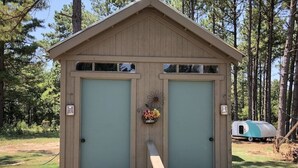 A wooden shed with two doors, a small flower arrangement, and a bench in front. - Spirit Warrior Tipi At Music Springs (Hawkins)