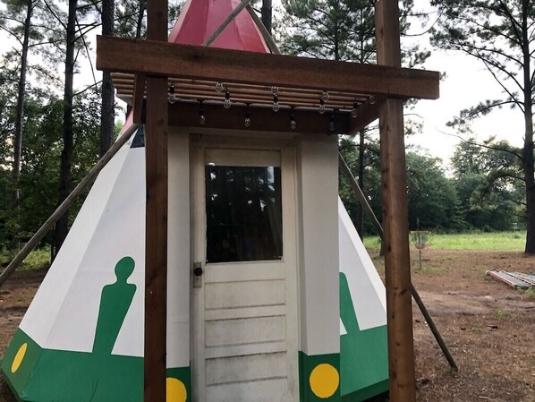 Una estructura pequeña y triangular con una puerta y una ventana, rodeada por un marco de madera y un techo rojo.
