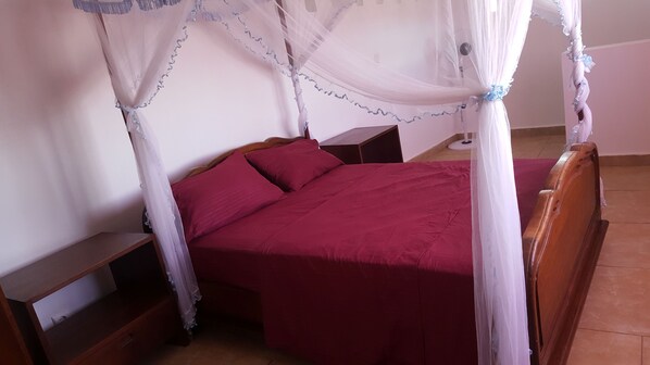 Una cama con dosel, cabecera de madera y colcha roja.