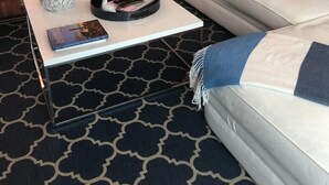 A modern living room with a white sofa, a coffee table with a book, and a patterned rug. - Beautiful Ormond Beach Oceanview Condo (Ormond Beach)