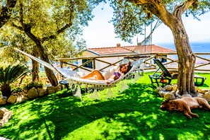 A hammock in a lush garden with a house in the background.