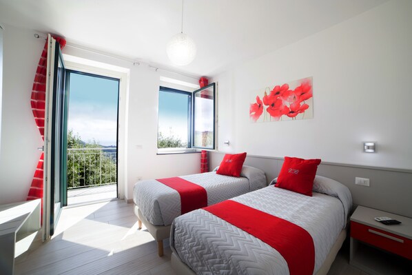A modern hotel room with two beds, a balcony, and a large window offering a city view.
