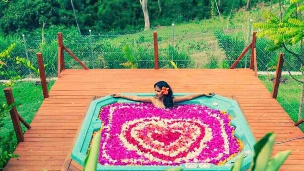 Una persona sentada en una terraza de madera con un arreglo floral en forma de corazón.