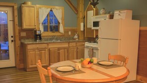 Una cocina con armarios de madera, una estufa y un refrigerador. Hay una mesa de comedor con sillas y un frutero.
