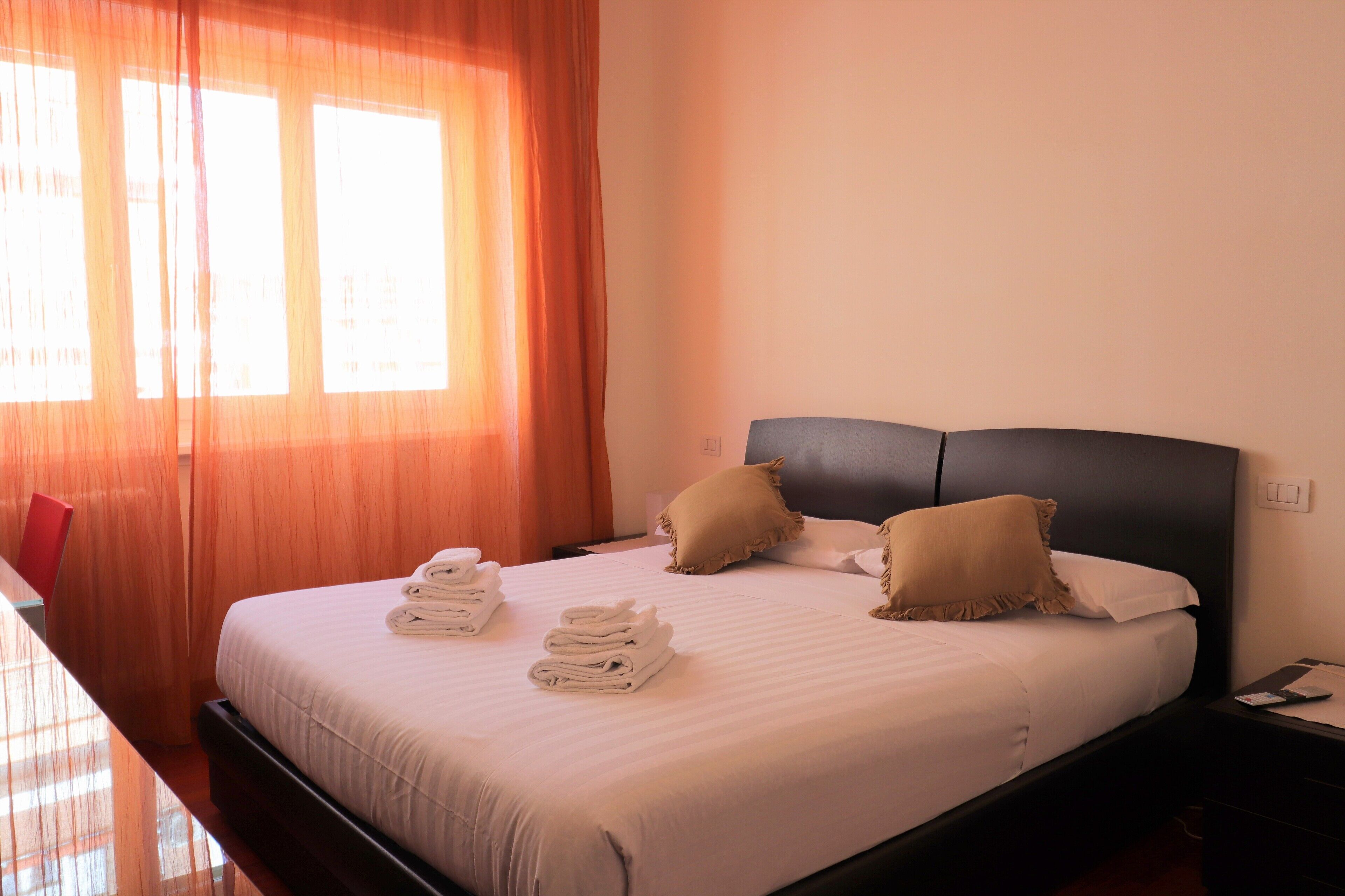 A neatly made bed with folded towels, a dark headboard, and two pillows.