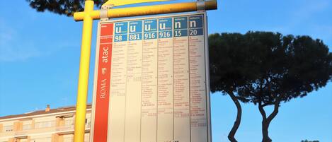 A bus stop sign with bus route information and a yellow pole.