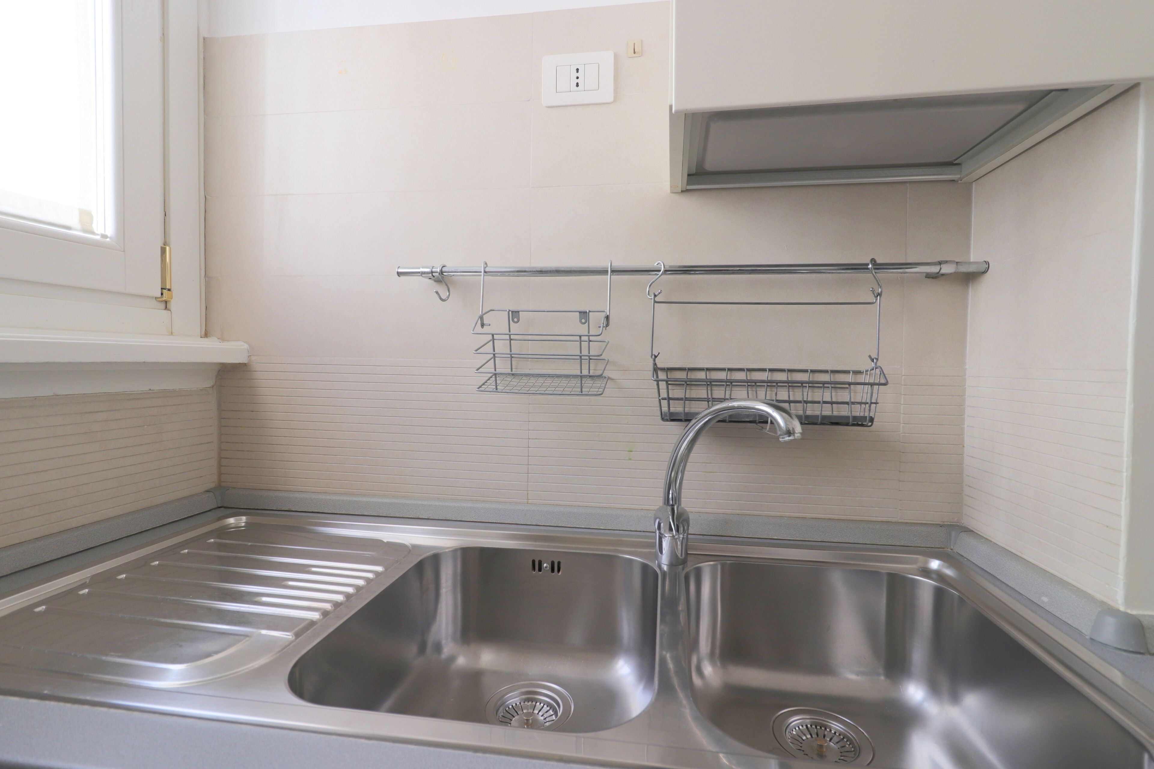 A kitchen with two stainless steel sinks, a window, and a wall-mounted rack with shelves.