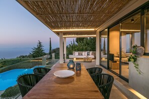 A modern outdoor dining area with a wooden table, chairs, and a view of the ocean.
