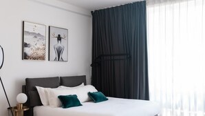 Ein modernes Schlafzimmer mit einem großen Bett, dunklen Vorhängen und zwei an der Wand befestigten Kunstwerken.