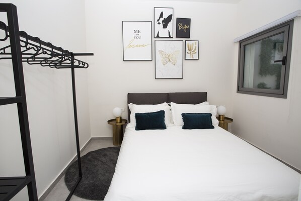 A neatly arranged bedroom with a bed, a hanging clothes rack, and framed artwork on the wall. - Emilia TLV (Tel Aviv)