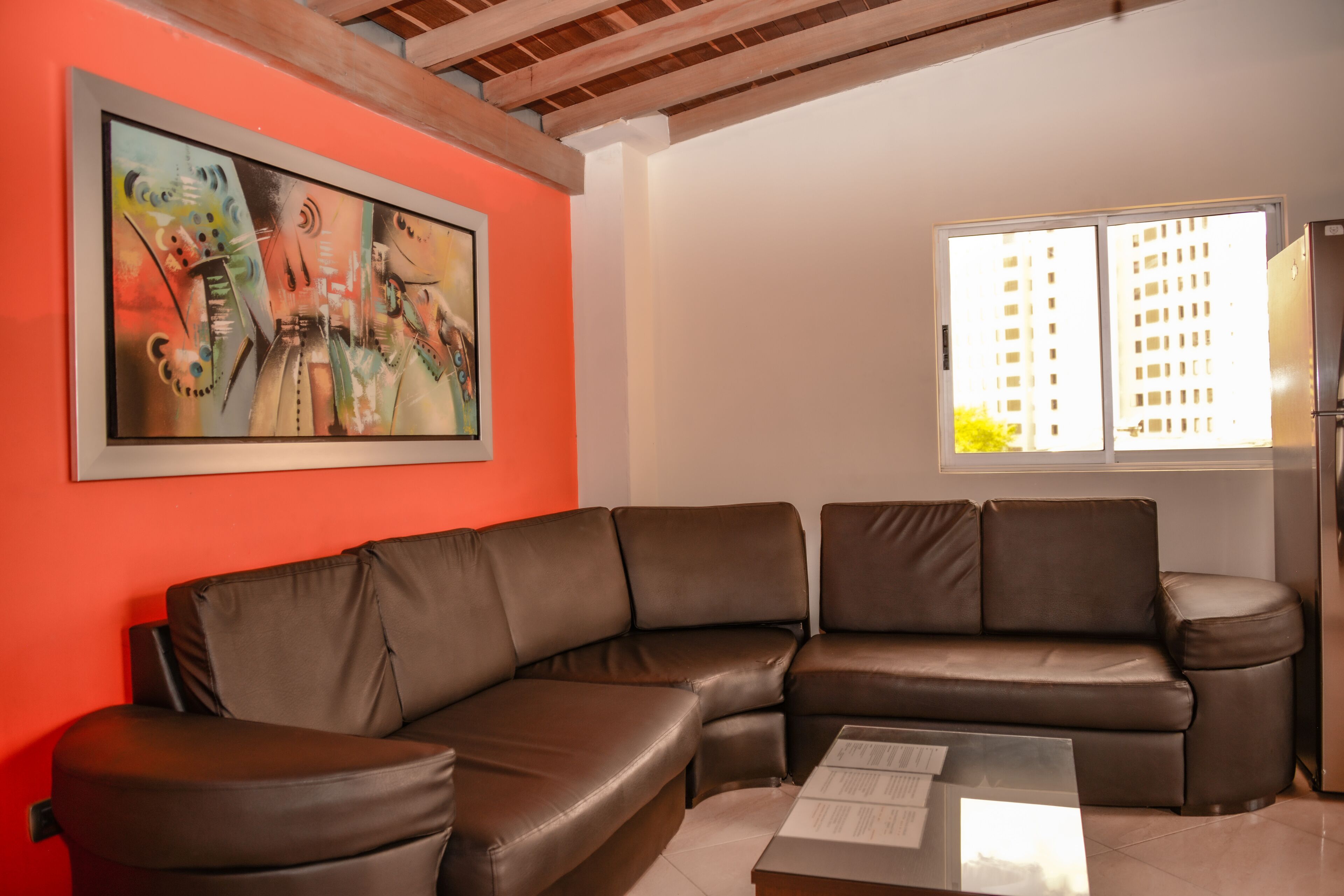 A living room with a brown leather sectional sofa, a glass coffee table, and a painting on the wall.