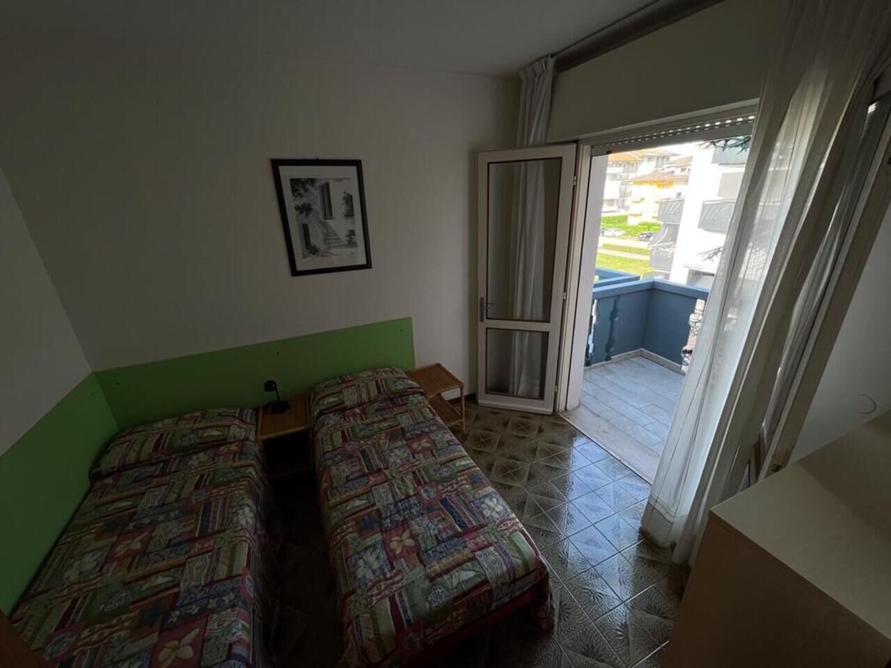 A room with two beds, a small table, a framed picture on the wall, and a sliding glass door leading to an outdoor area.