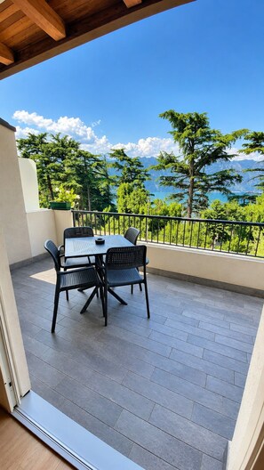 Ein Balkon mit Tisch und Stühlen, mit Blick auf eine Berglandschaft und ein Gewässer.