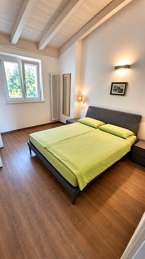Ein Schlafzimmer mit einem Bett, einem Fenster, einem Heizkörper und einer Wandleuchte.