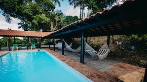 Una piscina con plataforma de azulejos, hamacas y sillas verdes.