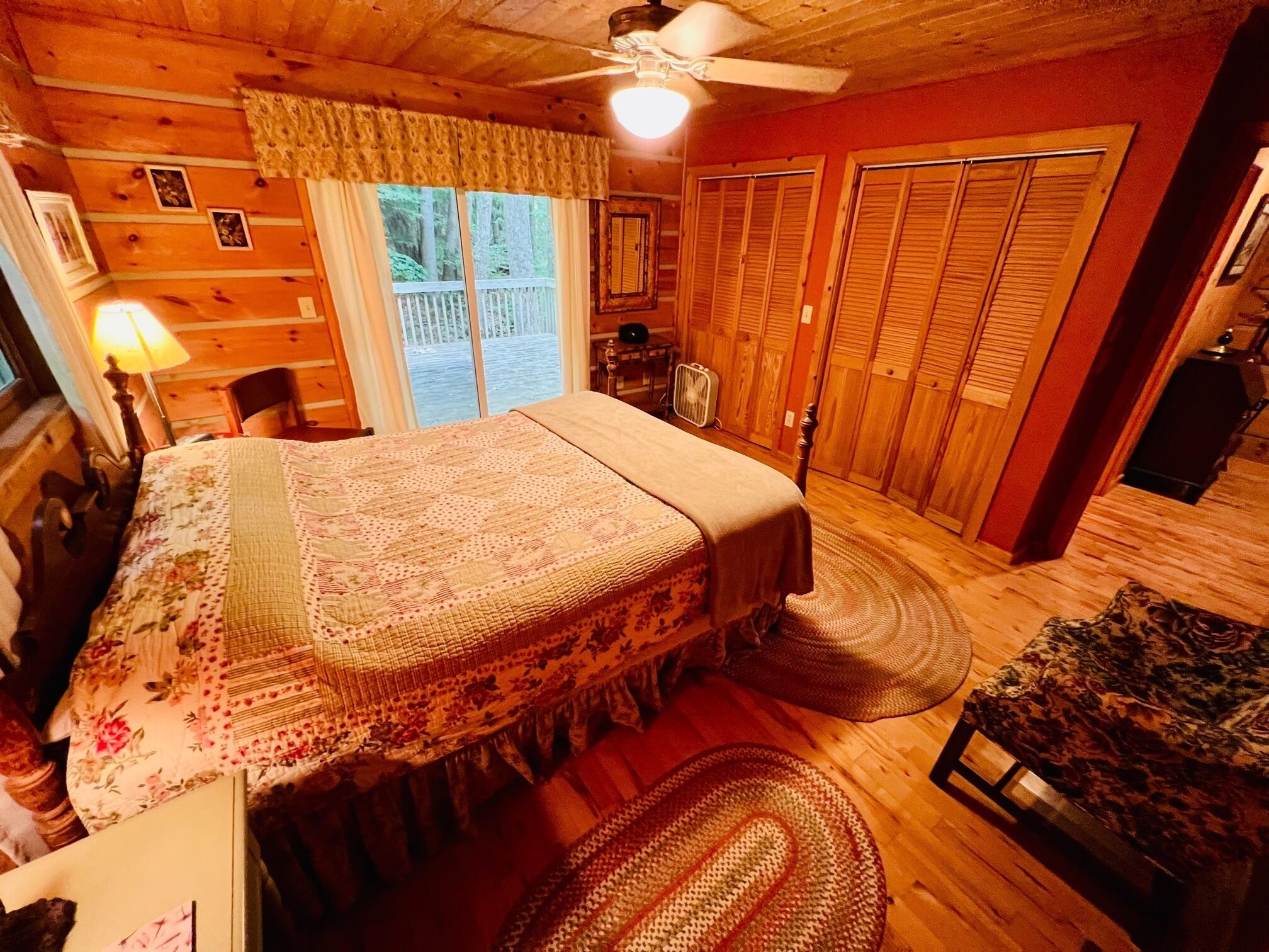 A cozy room with a bed, wooden walls, a ceiling fan, and a view of the outdoors.