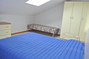Une petite chambre avec un lit simple, un plafond en pente et un puits de lumière, une armoire et une table de chevet.