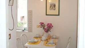 A dining area with a white table set for four, white chairs, a vase with pink flowers, and a framed picture on the wall. - Rome-Trastevere. Ideally located. All within walking distance. Internet (Rome)
