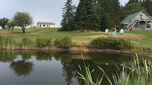 A serene lakeside setting with a small house, a larger building with a green roof, and a dock extending into the water.