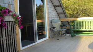 A wooden deck with a sliding glass door, a green bench, and a chair.