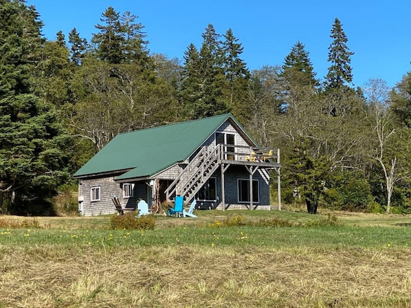 A rustic cabin with a green roof, wooden exterior, and a balcony with yellow chairs.