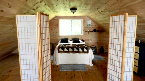 A cozy attic bedroom with a bed, a window, and wooden walls.