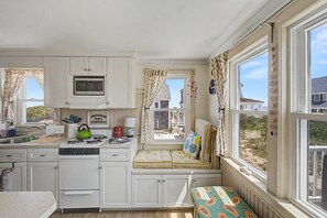 Une cuisine équipée d’un four à micro-ondes encastré, d’une cuisinière à gaz et d’un coin fenêtre agrémenté de coussins.