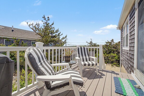 A deck with two striped chairs, a small table, and a potted plant.